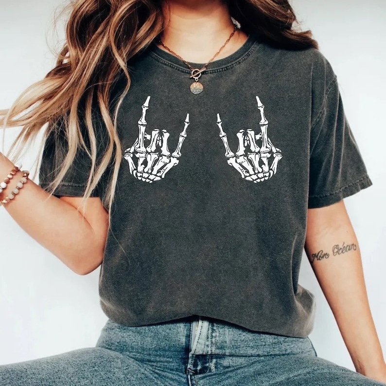 K&ouml;nnte beinhalten: Ein dunkelgraues T-Shirt mit einem wei&szlig;en Skelett-Hand-Motiv, das die Rock'n'Roll-Handgeste macht. Das Shirt ist cropped und hat eine lockere Passform.