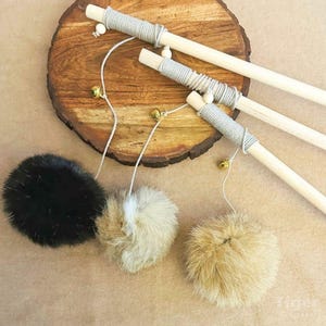 May include: Three cat toys with fluffy pom-poms in black, white, and brown, attached to wooden sticks with string and bells.