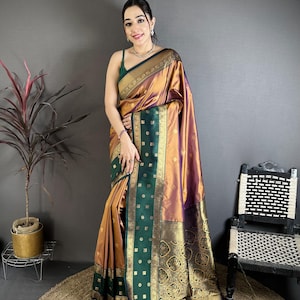 Könnte beinhalten: Eine Frau trägt einen traditionellen indischen Sari. Der Sari hat eine Mischung aus Gold-, Lila- und Grüntönen mit aufwendigen Goldmustern. Der Saum ist dunkelgrün mit goldenen Details. Der Sari ist elegant drapiert.