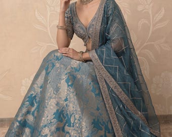 May include: A teal and silver embroidered lehenga, a traditional Indian garment, featuring a matching dupatta. The lehenga has a detailed floral and animal pattern. The outfit includes a matching blouse and jewelry.