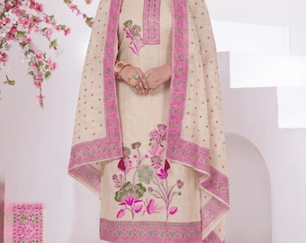 May include: A beige salwar kameez ensemble with pink floral embroidery and trim. The outfit includes a tunic, pants, and a matching scarf. The scarf is draped over the head and shoulders. The outfit is worn with matching shoes.