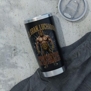 May include: Black insulated tumbler featuring a luchador design with the text "EL GRAN LUCHADOR" and "PROTECTOR DE LA FAMILIA". The tumbler has a silver rim and a clear lid. The luchador is depicted in a mask and wrestling attire.