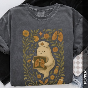May include: Dark gray sweatshirt featuring a cartoon ghost nurse holding an X-ray of lungs. The design includes yellow flowers, a stethoscope, and medicine bottles. The ghost wears a nurse's cap with a cross.