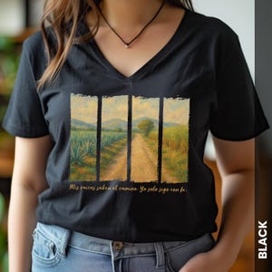 Può includere: T-shirt nero con scollo a V con un design paesaggistico che mostra uno sterrato, campi e montagne. La maglietta include il testo "Mis raíces saben el camino. Yo solo sigo con fe."