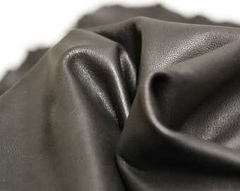 May include: Close-up of a black leather fabric with a textured surface. The fabric is folded and draped, showing its soft and supple texture.