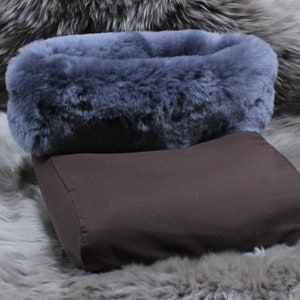 May include: A pet bed featuring a dark brown base and a fluffy, grey-blue faux fur rim. The bed is set against a backdrop of grey faux fur, creating a cosy and inviting aesthetic. The design suggests comfort and warmth for a small animal.