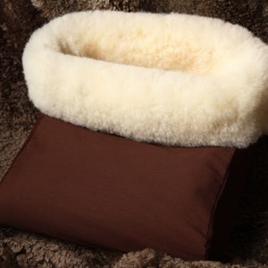 May include: A brown fabric dog bed with a white sheepskin lining. The bed is shaped like a crescent moon and has a raised edge.