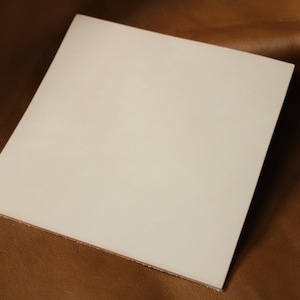 May include: A white leather sheet, smooth and unblemished, lies on a brown surface.