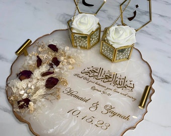 May include: A decorative white and gold resin tray with gold handles, featuring floral arrangements and two glass boxes with white roses. The tray includes Arabic calligraphy and the names "Hemaid & Zaynah" with a date.