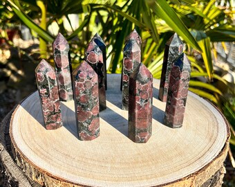 May include: A collection of ten black and red gemstone points, also known as red and black jasper, arranged on a wooden surface. The points are all roughly the same size and shape, and they have a natural, unpolished finish.
