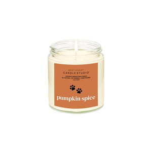 May include: A clear glass jar candle with a white wax interior. The label is orange with the text "WEST COAST CANDLE STUDIO" and "pumpkin spice". Includes paw prints and the words "COCONUT APRICOT WAX CANDLE".
