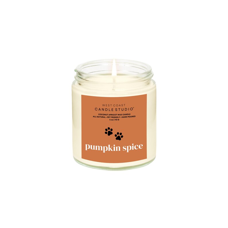 May include: A clear glass jar candle with a white wax interior. The label is orange with the text "WEST COAST CANDLE STUDIO" and "pumpkin spice". Includes paw prints and the words "COCONUT APRICOT WAX CANDLE".