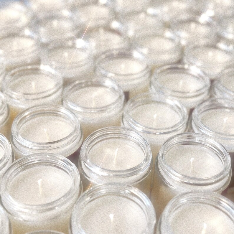 May include: A collection of small, clear glass jar candles with white wax and centered wicks. The candles are arranged closely together, creating a repetitive pattern. The image has a soft, diffused lighting.