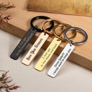 Può includere: Quattro portachiavi rettangolari di diversi colori. I colori sono nero, beige, oro e bianco. I messaggi includono "I love you to the moon and back", "Love You Forever" e "Drive Safe!!! I kinda want to keep you".