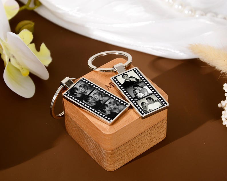 Op de afbeelding: Twee rechthoekige metalen sleutelhangers met een zwart-wit filmstripontwerp. Elke sleutelhanger toont een reeks kleine, zwart-wit foto's van een koppel binnen de rand van de filmstrip, bevestigd aan een ronde metalen ring.