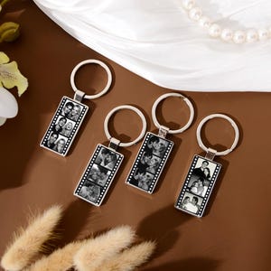 Op de afbeelding: Vier rechthoekige metalen sleutelhangers, elk voorzien van een verticale strook zwart-witfoto's gerangschikt als een filmrol. Elke sleutelhanger heeft een zilverkleurige metalen ring aan de bovenkant voor het bevestigen van sleutels.