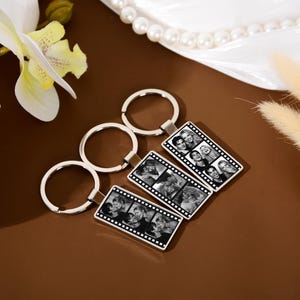 Op de afbeelding: Drie rechthoekige zilverkleurige metalen sleutelhangers met een zwart-wit filmstripontwerp. Elke sleutelhanger toont een reeks kleine, vierkante zwart-witfoto's van mensen die verticaal in de rand van de filmstrip zijn gerangschikt.