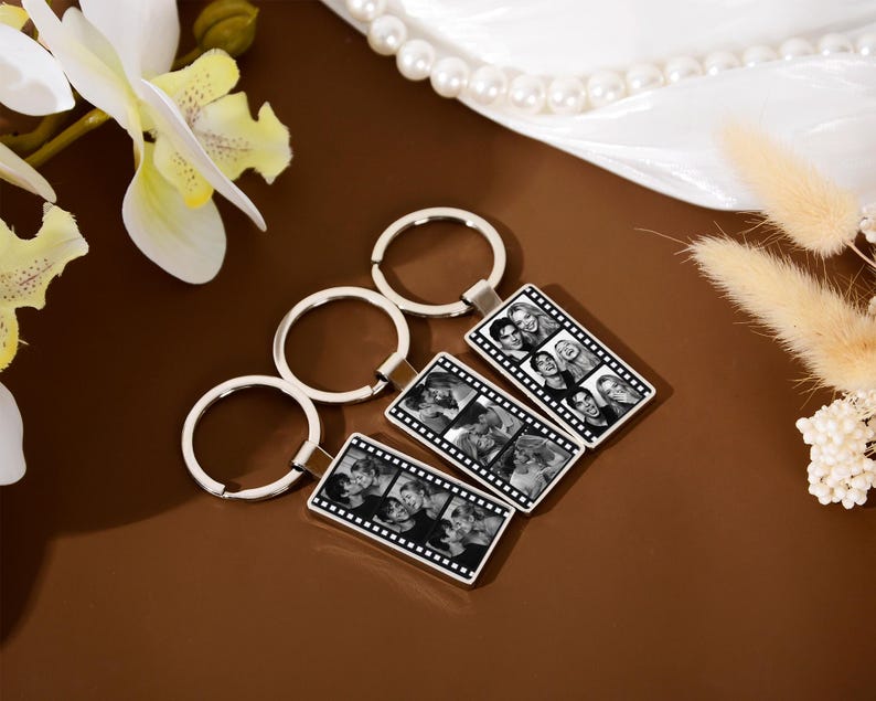 Op de afbeelding: Drie rechthoekige zilverkleurige metalen sleutelhangers met een zwart-wit filmstripontwerp. Elke sleutelhanger toont een reeks kleine, vierkante zwart-witfoto's van mensen die verticaal in de rand van de filmstrip zijn gerangschikt.