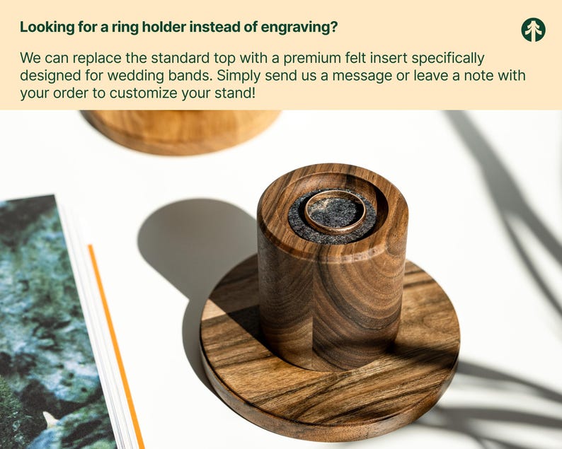 a wooden ring holder with a gold ring inside, placed on a wooden stand. The stand has a textured finish, and the ring holder appears to be made of wood. The background is white, and there is a green plant visible.