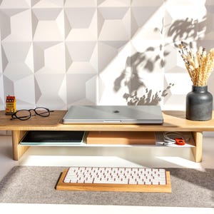 a wooden desk with a laptop, glasses, a vase with flowers, and a keyboard on it.