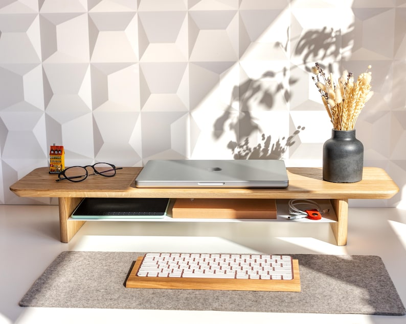 a wooden desk with a laptop, glasses, a vase with flowers, and a keyboard on it.