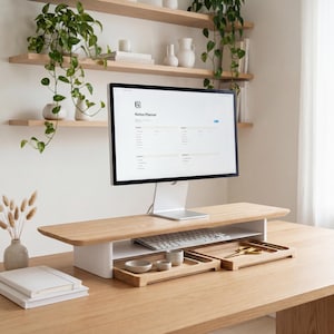a modern workspace with a computer monitor, keyboard, and mouse on a wooden desk. The desk has a wooden stand and a shelf above it, providing additional storage space. The desk also has a few decorative items, such as a potted plant, a vase, and a stack of books. The overall setting appears to be a well-organized and comfortable work environment.