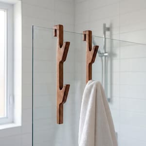 A wooden towel rack with two towel hooks attached to it, hanging in a bathroom with a glass shower door.