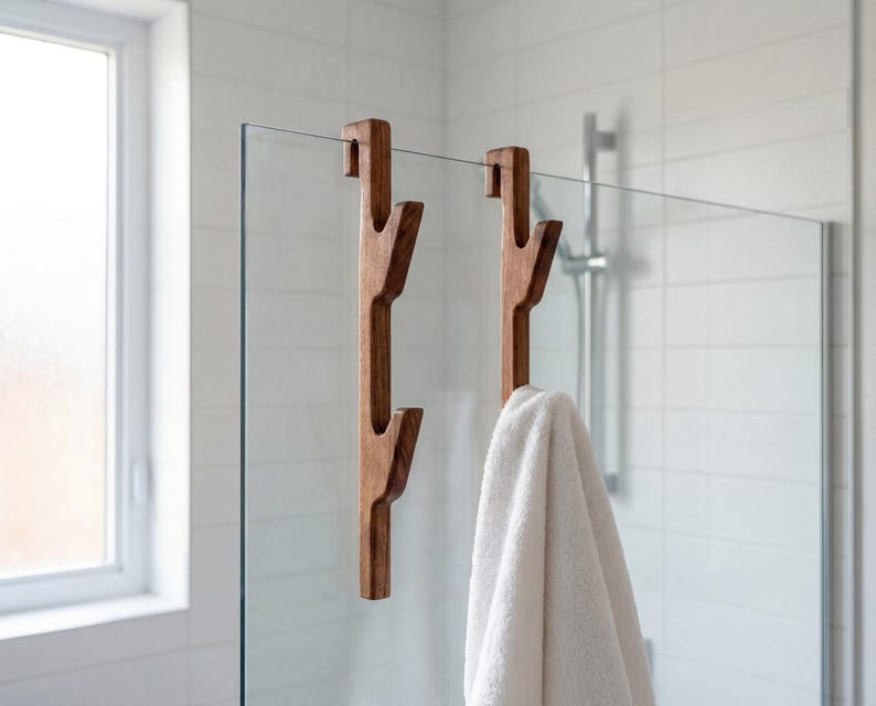 A wooden towel rack with two towel hooks attached to it, hanging in a bathroom with a glass shower door.