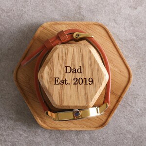 A wooden watch stand with a watch on it, and the text "Dad Est. 2019" engraved on the stand.