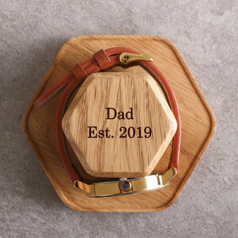A wooden watch stand with a watch on it, and the text "Dad Est. 2019" engraved on the stand.