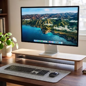 a desktop computer monitor displaying a scenic mountain landscape, with a keyboard and mouse on a wooden desk in front of it.