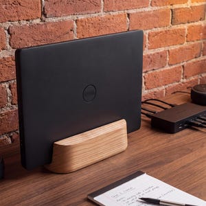a black laptop placed on a wooden desk, with a notebook and a pen nearby. The desk is set against a brick wall, creating a rustic and cozy atmosphere.