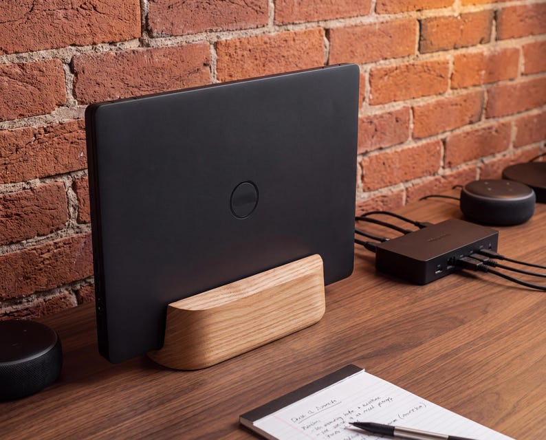 a black laptop placed on a wooden desk, with a notebook and a pen nearby. The desk is set against a brick wall, creating a rustic and cozy atmosphere.