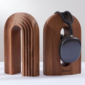 Peut inclure: Deux supports en bois pour casque audio, de couleur marron chaud. L'un est une arche pleine, l'autre a une découpe pour maintenir le casque. Une paire de casques noirs repose sur le second support. Les supports sont marqués du mot "Radwood".