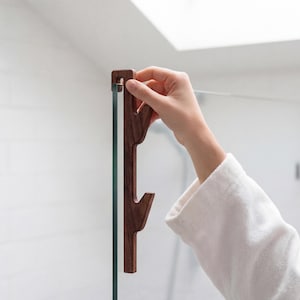 A person's hand is holding a wooden object, which appears to be a handle or a tool, in front of a glass door or window.