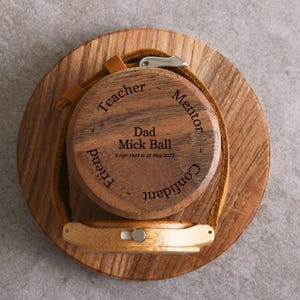 A wooden watch stand with a wooden case featuring engraved text and a watchband.