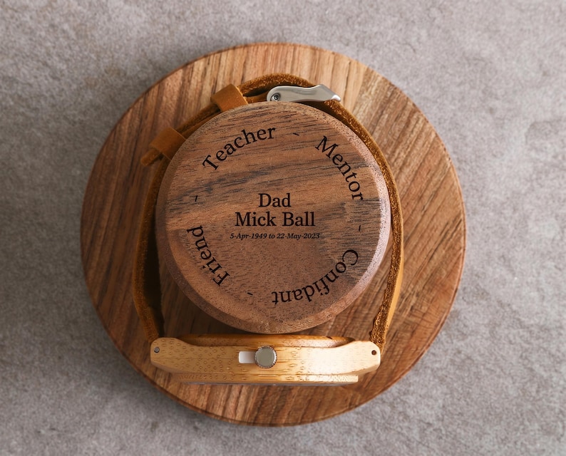 A wooden watch stand with a wooden case featuring engraved text and a watchband.
