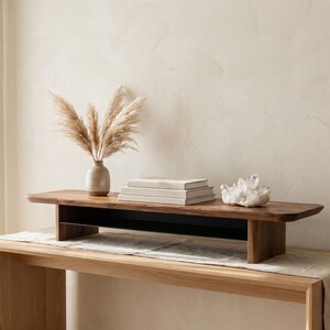 a wooden table with a vase of dried flowers, a stack of books, and a crystal on it, set against a plain white wall.