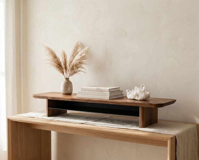 a wooden table with a vase of dried flowers, a stack of books, and a crystal on it, set against a plain white wall.