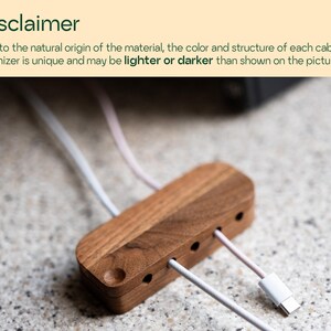 a wooden cable organizer with multiple white cables plugged into it, placed on a speckled surface.