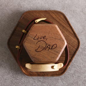 A wooden box with a watch strap attached to it, and the words "Love, Dad" written on the box.