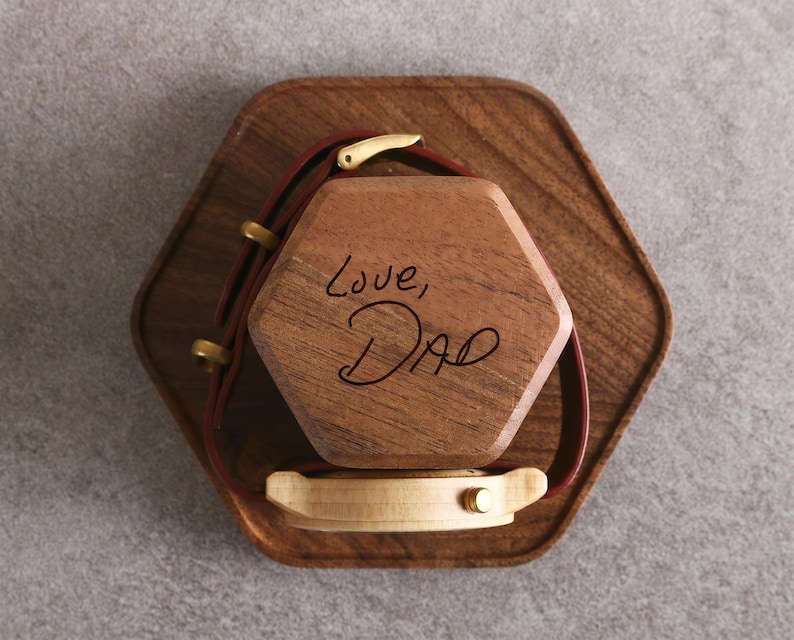 A wooden box with a watch strap attached to it, and the words "Love, Dad" written on the box.
