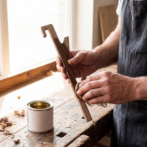 A person is working on a wooden object, likely a tool or piece of furniture, in a workshop setting.