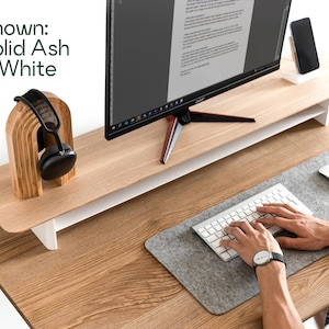 a person working at a desk with a computer monitor, keyboard, and headphones. The desk has a wooden stand and a gray mouse pad.
