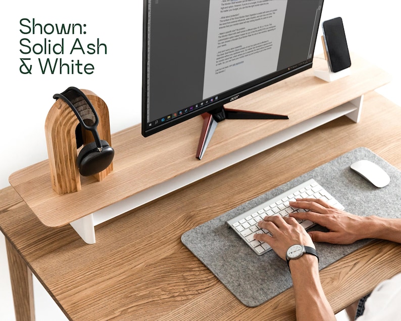 a person working at a desk with a computer monitor, keyboard, and headphones. The desk has a wooden stand and a gray mouse pad.