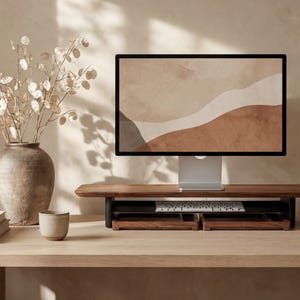 a wooden desk with a computer monitor, keyboard, and a vase with white flowers. The desk is set against a beige wall, and there is a cup and a book on the desk as well.