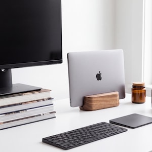 a well-organized workspace with a computer monitor, a laptop, a keyboard, and a stack of books. There is also a jar and a cup on the desk.