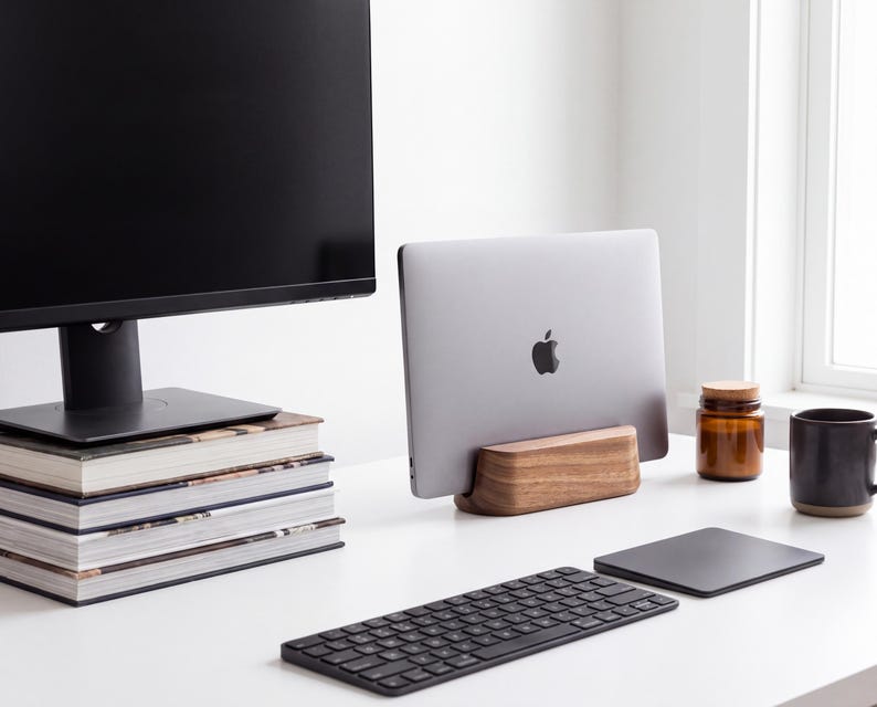 a well-organized workspace with a computer monitor, a laptop, a keyboard, and a stack of books. There is also a jar and a cup on the desk.