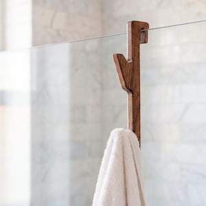 A wooden towel rack with a white towel hanging on it, mounted on a glass wall in a bathroom.