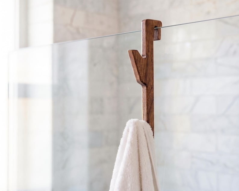 A wooden towel rack with a white towel hanging on it, mounted on a glass wall in a bathroom.